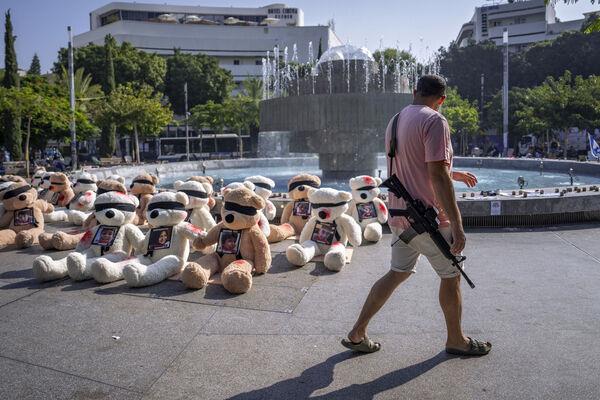 An off-duty Israeli soldier walks by an installation of blindfolded giant teddy bears adorned with photos of Israelis held captive in Gaza, in Tel Aviv, Israel. The installation is meant to draw attention to over 200 people who were abducted by Hamas militants during a bloody and unprecedented Oct. 7 cross-border attack. 
