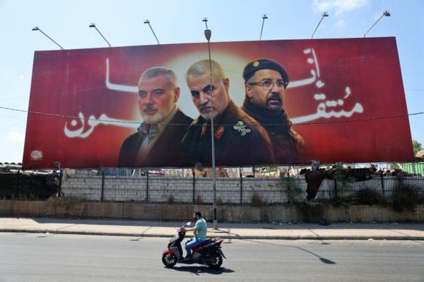 TOPSHOT - A man rides his moped past a billboard bearing portraits of slain leaders, Ismail Haniyeh of the Palestinian militant group Hamas, Iranian Quds Force chief Qasem Soleimani (C), and Hezbollah senior commander Fuad Shukr on the main road near the Beirut International Airport on August 3, 2024. (Photo by Ibrahim AMRO / AFP)